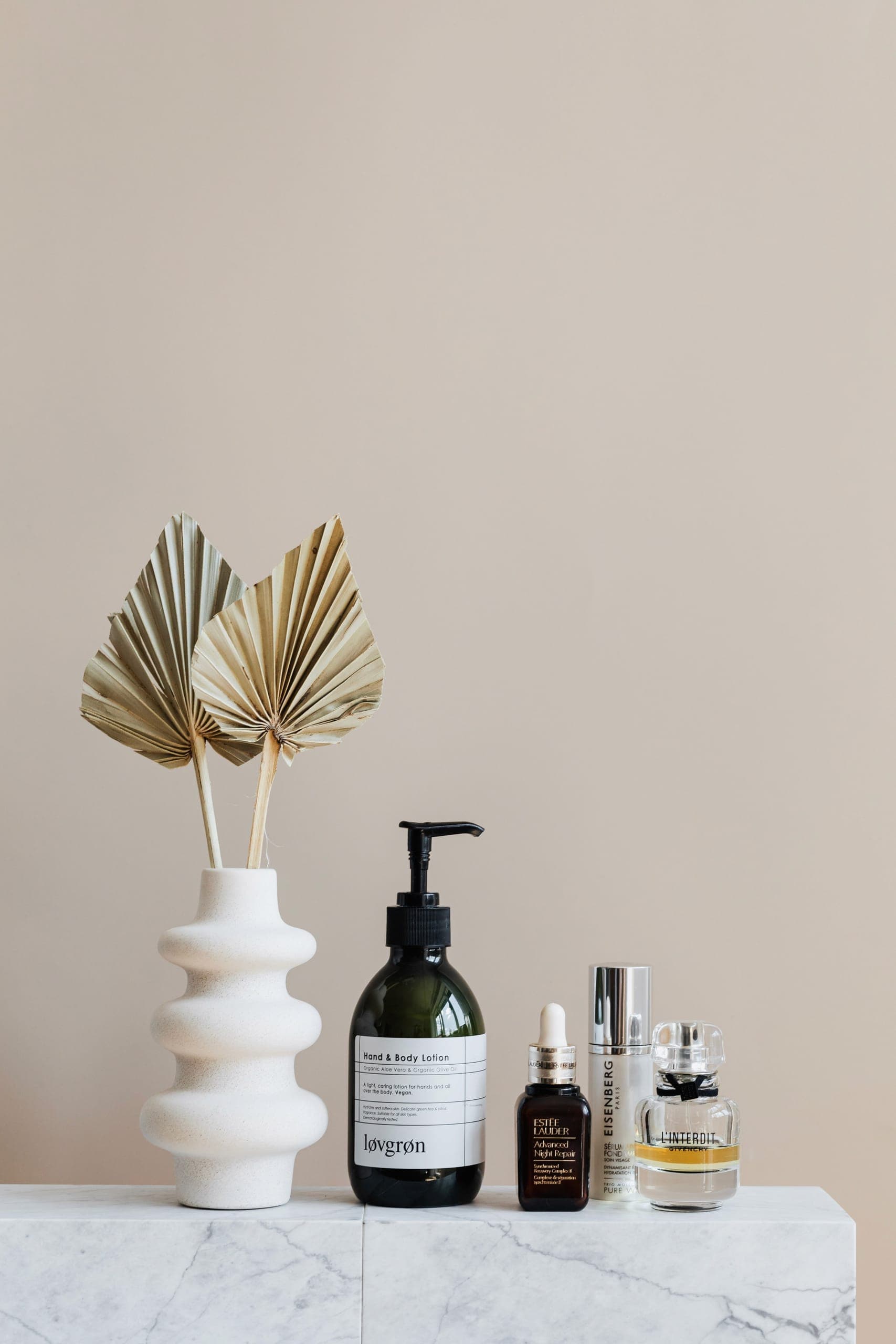 Beautyproducten op een marmeren plateau tegen een beige wand