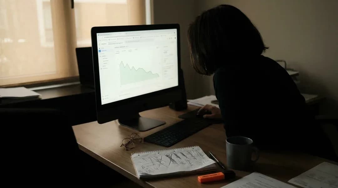 Iemand bekijkt in een donker kantoor een analytics-dashboard met een dalende grafiek, met doorgestreepte notities op het bureau