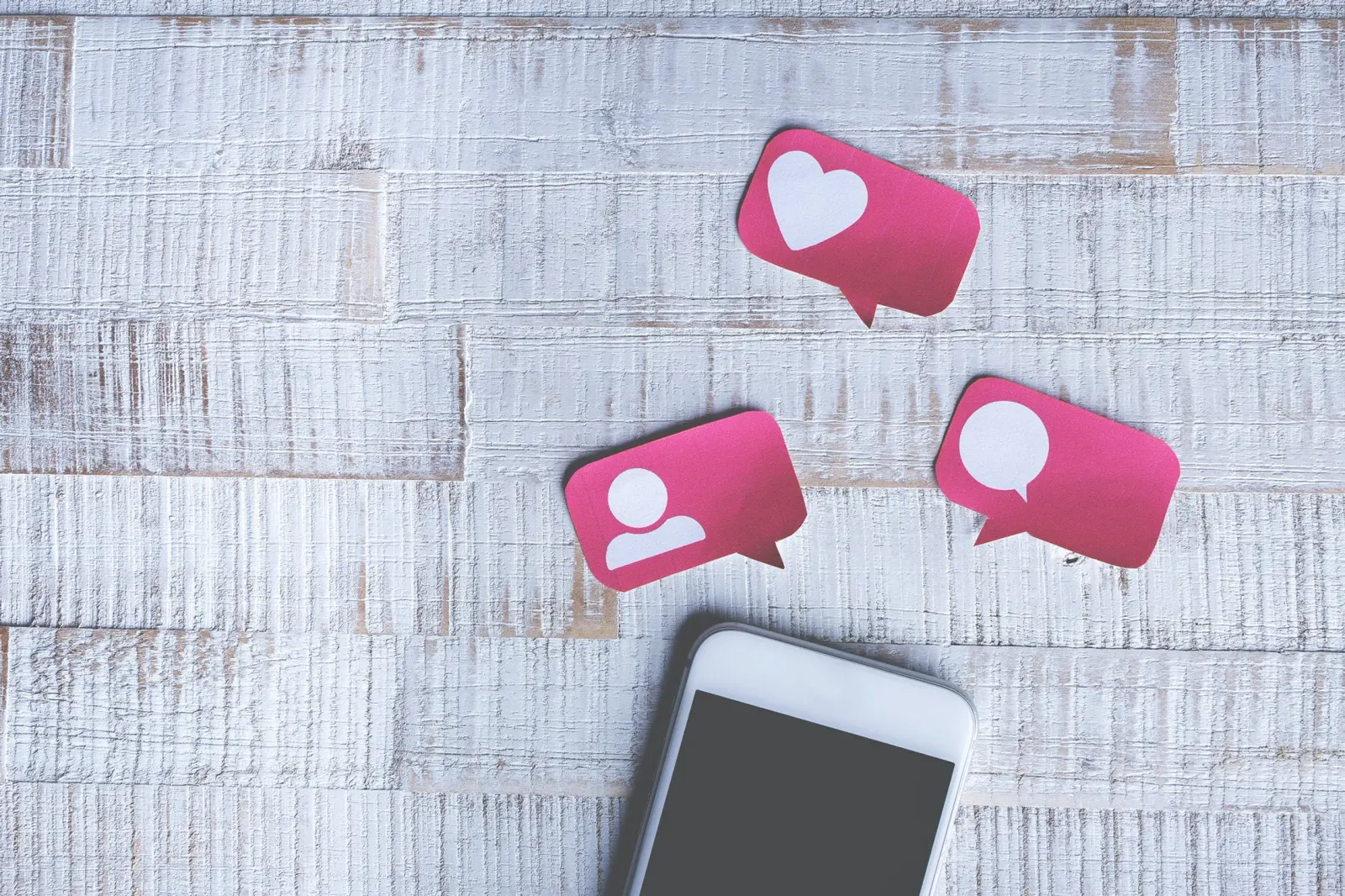 Smartphone op een houten ondergrond met daarboven papieren social-media-iconen voor likes, volgers en reacties